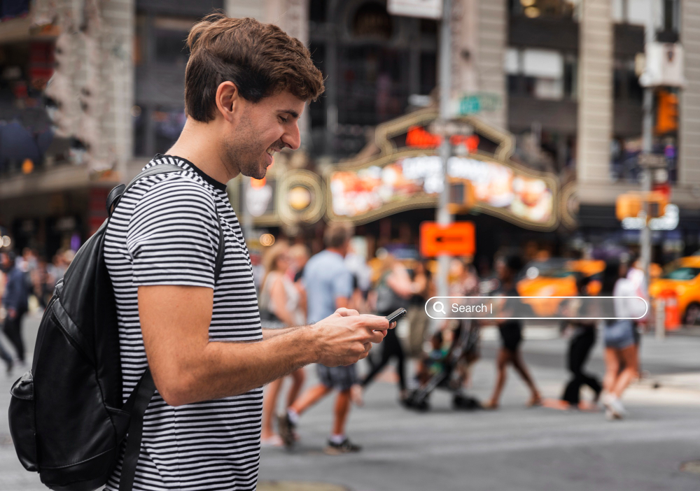 A man stands in the center of a bustling city street, surrounded by tall buildings and urban activity